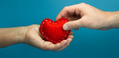 Caregiver concept. Man hand puting the red soft heart in woman hand on blue background