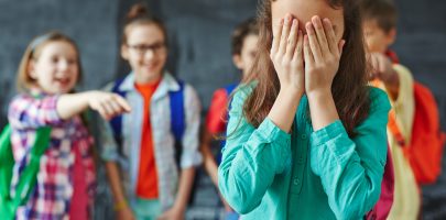 Schoolgirl crying on background of classmates teasing her